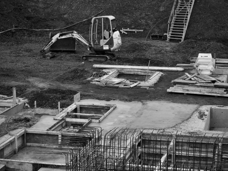 Fundamente mit Schalung und Bewehrung auf einer Baustelle, dahinter ein Minibagger