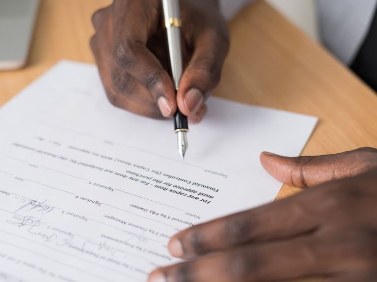 Eine Hand unterschreibt ein Formular mit mehreren Unterschriftszeilen