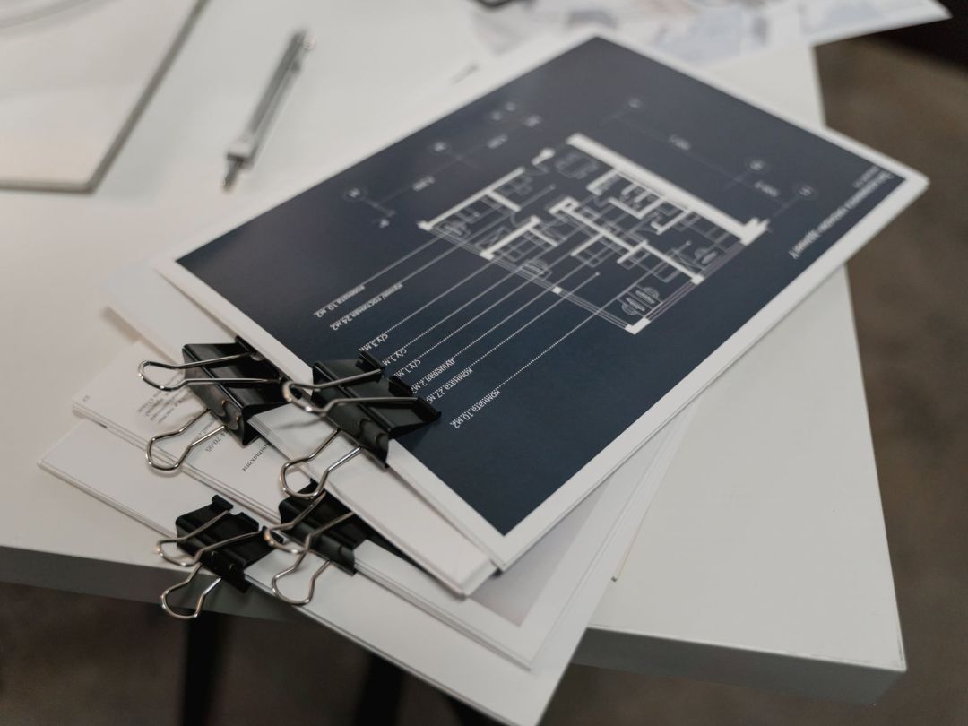 Geheftete Plansätze auf einem Arbeitstisch, auf dem obersten Blatt ein Grundriss mit Bemaßung